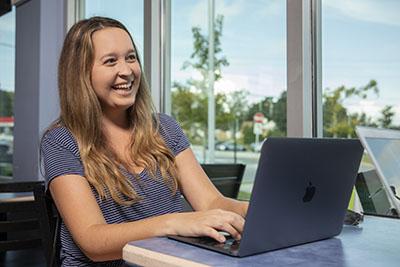 一名UWF学生在室内使用笔记本电脑时微笑着.